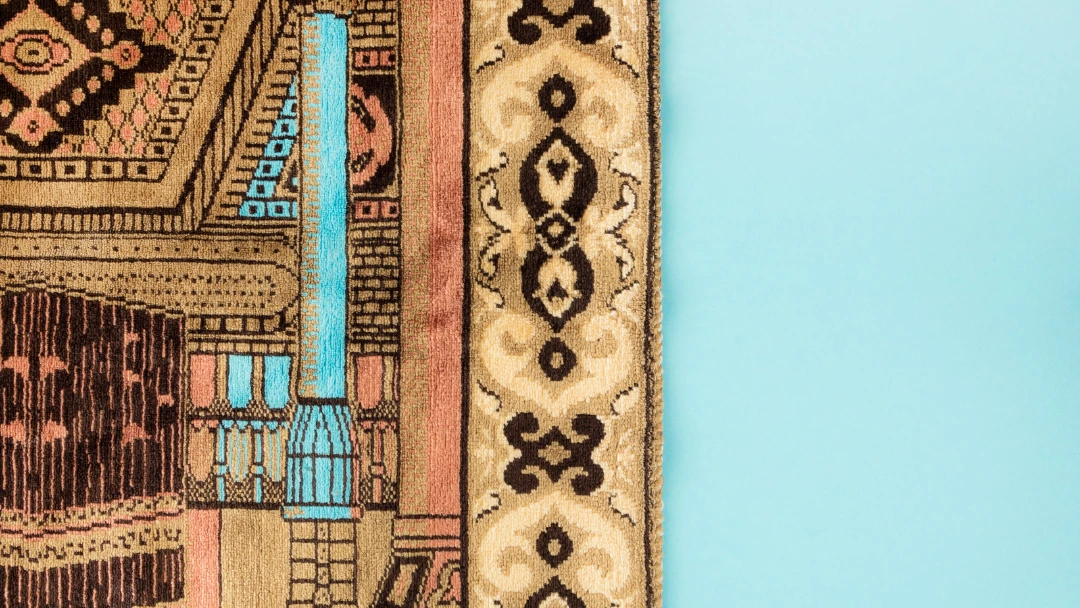 Détail de tapis oriental aux couleurs ravivées après nettoyage professionnel sur fond bleu clair.